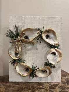 an oyster shell wreath with pine needles on a white board, hanging on the wall