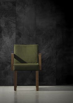 a green chair sitting in front of a black wall with a shadow cast on it