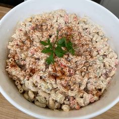 a white bowl filled with macaroni salad and topped with green leafy garnish