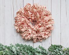 a red and white striped wreath hanging on the side of a wooden wall next to green plants