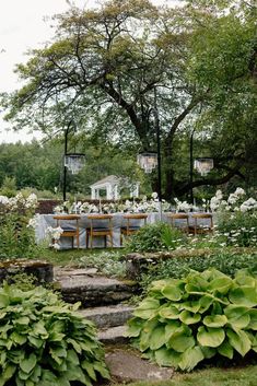 an outdoor dining area with tables and chairs surrounded by greenery, flowers and trees