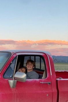 a young man sitting in the driver's seat of a red pick up truck