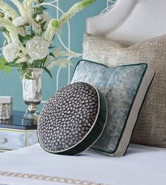 a white bed topped with pillows next to a vase filled with flowers