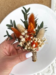 a hand holding a dried flower arrangement on a plate