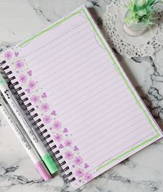 a notepad and two pens sitting on top of a marble counter next to a vase with flowers