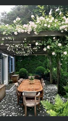 a wooden table sitting under a pergoline covered arbor with white flowers on it