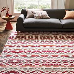 a living room with a gray couch and colorful rugs on the floor in front of a window