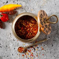 a small metal bowl filled with spices next to two spoons and some chili peppers