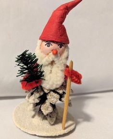 a small gnome holding a christmas tree on top of a white surface