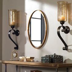 a wooden table topped with a mirror next to a wall mounted clock and candle holders