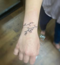 a small tattoo on the wrist of a woman's left hand, with flowers and leaves