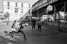 a group of young men playing a game of basketball on an outdoor court with buildings in the background