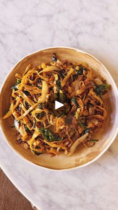 a wooden bowl filled with noodles and vegetables on top of a white marble countertop