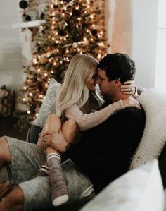 a man and woman sitting on a couch in front of a christmas tree