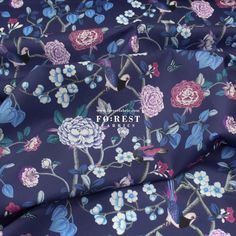 the fabric has flowers on it and is blue with pink, purple and green leaves