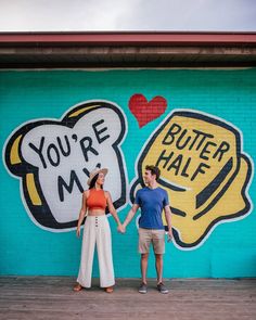 a man and woman holding hands in front of a wall painted with cartoon character images