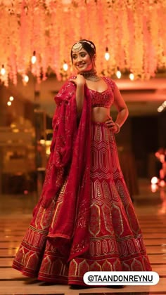 a woman in a red and gold lehenga standing on the floor with chandelier