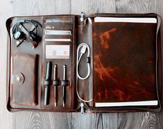 an open brown leather case with various items in it on a wooden table next to a pair of headphones