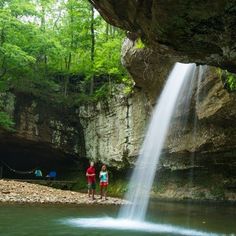 two people are standing in front of a waterfall and looking at the water from below