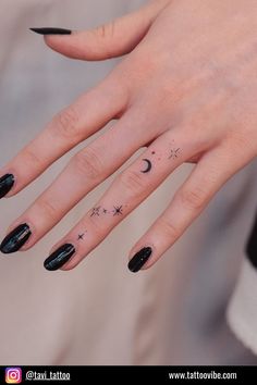 a woman's hand with black nail polish and stars on her fingers, while she is wearing a crescent moon tattoo