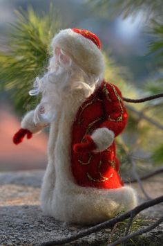 a small santa clause figurine sitting on top of a stone ground next to a pine tree