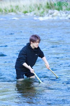 a boy in the water holding a stick with both hands and crouching down to catch something