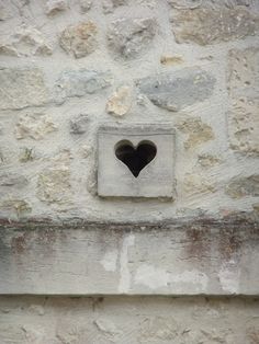 a heart shaped hole in the side of a stone wall with a small window on it