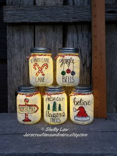 painted mason jars with sayings on them sitting in front of a wooden fence and measuring tape