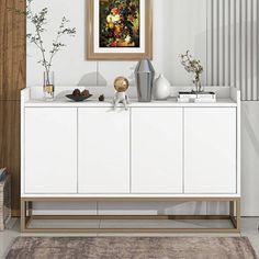 a white sideboard with vases and plants on it in front of a painting