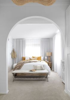 a bedroom with white walls and carpeted flooring has an arch leading to the bed