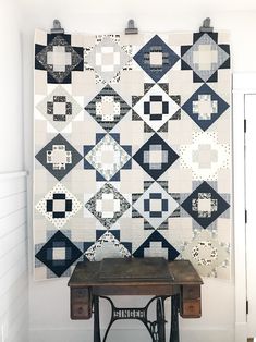 an old sewing machine sitting in front of a quilted wall hanging on the wall