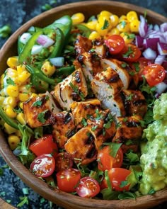 a wooden bowl filled with chicken and veggies next to guacamole