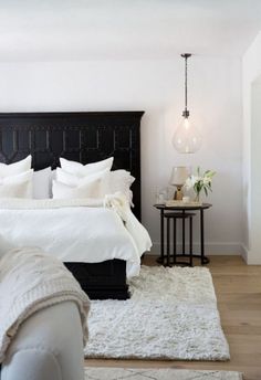 a bedroom with white bedding and black headboard, rugs on the floor