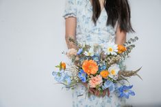 a woman holding a bouquet of flowers in her hands and wearing a blue floral dress