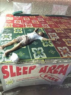 a man laying on top of a green and red mattress covered in plastic wrap next to a sign that says sleep area