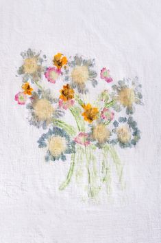 a vase filled with yellow and pink flowers on top of a white table cloth covered in crinkle paper