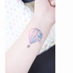 a small hot air balloon tattoo on the left inner arm and wrist, with pastel colors