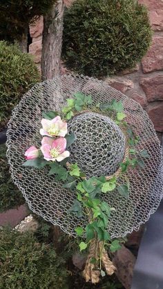 a hat with flowers on it sitting in front of a tree and bushes, next to a stone wall