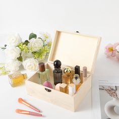 an open wooden box with cosmetics and flowers on the table next to it, along with other items