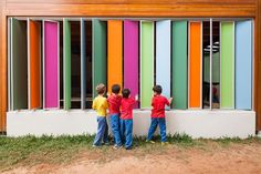 three children are standing in front of a multicolored building with their hands on the wall