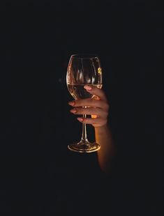 a woman's hand holding a wine glass in the dark