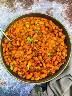 a bowl filled with beans and meat on top of a table next to a napkin