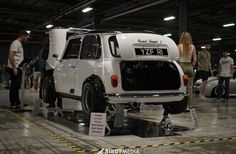 people standing around and looking at an old white car in a garage with other cars