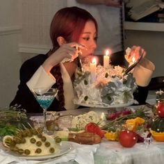 a woman sitting at a table with a cake in front of her and lit candles