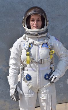 a woman in an astronaut suit standing next to a wall with her hands on her hips