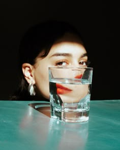 a woman sitting at a table with a glass of water in front of her face