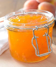 a glass jar filled with orange liquid sitting on top of a wooden table next to apples