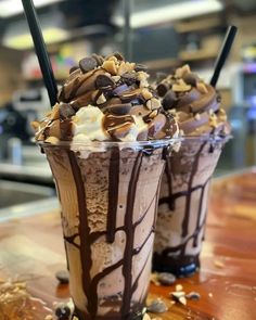 two ice cream sundaes with chocolate sauce and toppings on top, sitting on a table