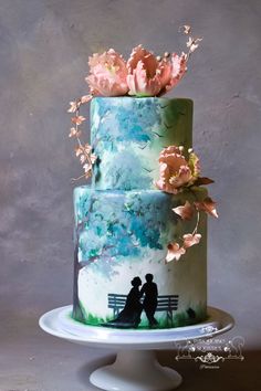 a wedding cake decorated with flowers and two people sitting on a bench