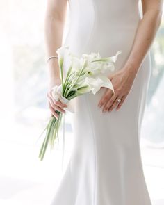 a woman in a white dress holding a bouquet of flowers and wearing a wedding ring